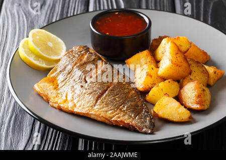 Fritti gustosi dorado filetto di pesce con patate guarnite e salse close-up su una piastra sul tavolo orizzontale. Foto Stock