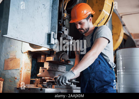 Ritratto di un giovane lavoratore in un elmetto in un grande impianto metalmeccanico. Il tecnico serve le macchine e produce componenti per apparecchiature a gas Foto Stock