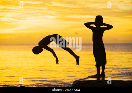 Un bambino si tuffa nel mare al tramonto su Funafuti, Tuvalu. Il mare è la loro casa e mentre essa fornisce la maggior parte del loro cibo in forma di pesce che anche t Foto Stock