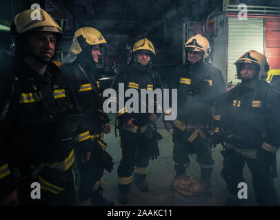 Team di vigili del fuoco in piedi all'interno di ( ) all'interno di un edificio accanto a un incendio del motore. Foto Stock