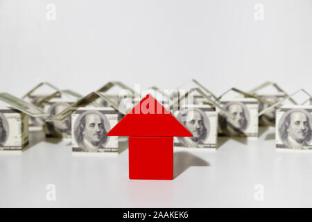Rosso blocco di legno casa con case fatte di dollari nel secondo termine su sfondo bianco Foto Stock