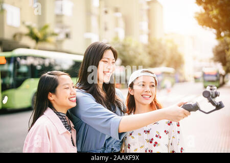 Felice Asian Girls rendendo storie di video nel centro della città - alla moda di giovani amici riprese con sospensione cardanica all'aperto dello smartphone Foto Stock