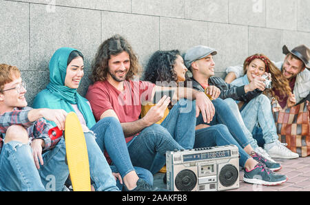 Gruppo di diversi amici divertendosi outdoor - la millenaria giovani utilizzando i telefoni cellulari e ascolto di musica con vintage stereo boombox Foto Stock