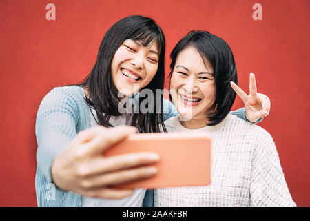 Asian madre e figlia prendendo foto selfie con mobile smartphone outdoor - felice famiglia cinese per divertirti con le nuove tendenze di applicazioni della tecnologia Foto Stock