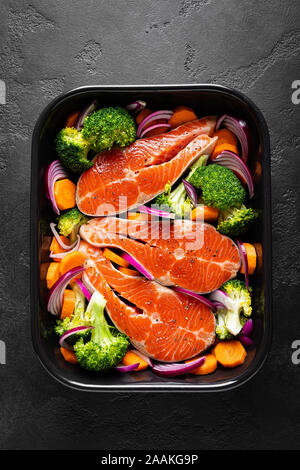 Salmone. La cottura crudo fresco salmone tranci di pesce con verdure, broccoli, la carota e la cipolla su sfondo nero, vista dall'alto Foto Stock