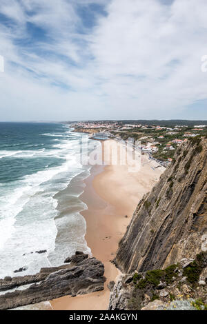 Vista dalla scogliera al di sopra della spiaggia di sabbia Praia Grande vicino a Sintra Portogallo in estate con le onde in rotolamento sotto il cielo nuvoloso Foto Stock