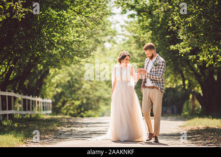 Coppie in viaggio di nozze gode di camminare nei boschi. Sposi abbraccio e tenere le mani. Gli sposi a piedi in avanti tenendo in mano il parco lungo il percorso nella soleggiata Foto Stock