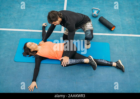 Montare la giovane donna facendo esercizi di stretching dopo un allenamento con personal trainer. Foto Stock