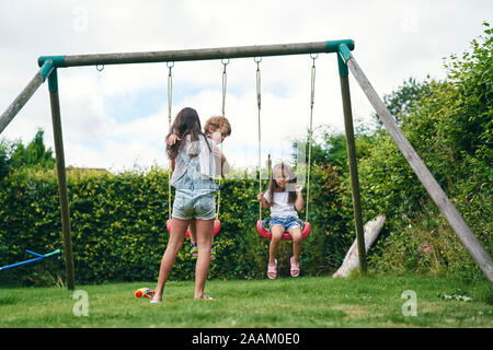 Ragazza trasporto bambini e guardare i giovani i gemelli su swing Foto Stock