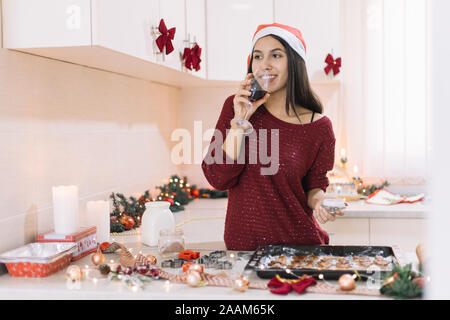 Signora sorridente bere il vino e la decorazione di gingerbread cookie Foto Stock