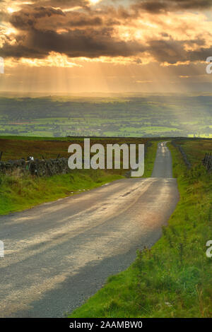 Country Road andando a distanza con raggi crepuscolari nel cielo, Pennines, Cumbria, England, Regno Unito Foto Stock