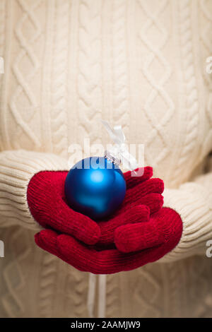 Donna che indossa stagionale muffole Rosso Blu Holding ornamento di Natale. Foto Stock