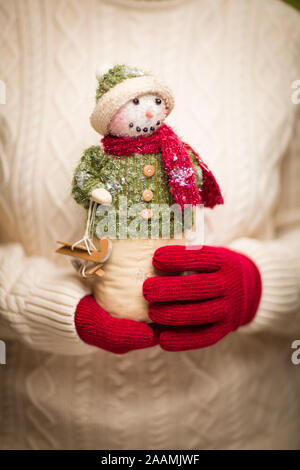 Donna che indossa rosso stagionale Mittens Holding Natale pupazzo di neve. Foto Stock