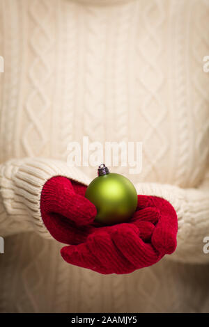 Donna che indossa rosso stagionale Mittens Holding Green ornamento di Natale. Foto Stock