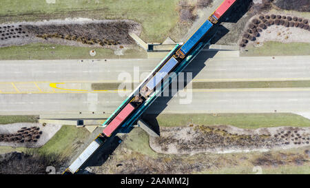 Un drone / vista aerea di un treno trasporta i contenitori di spedizione andando su una strada. Foto Stock