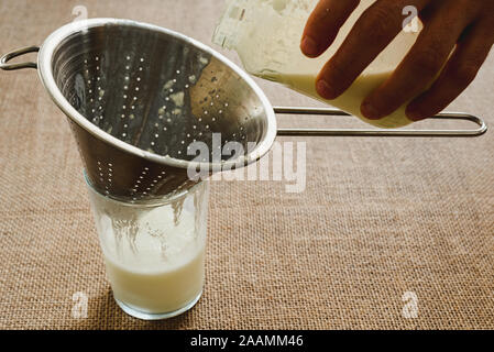 Mano d'uomo versa il latte il kefir in una caraffa per preparare una colazione sana per il microbiota intestinale. Foto Stock