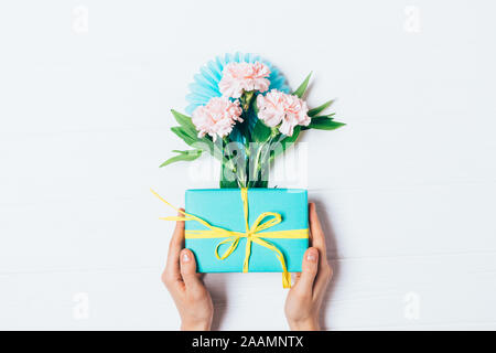 Piano di composizione laici confezione regalo in mani femminili accanto al bouquet di fiori su fondo bianco, vista dall'alto. Foto Stock