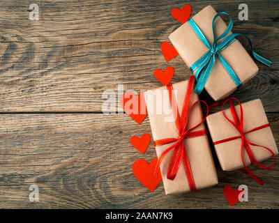 Il giorno di San Valentino sfondo. Doni avvolto con Kraft carta marrone, con nastri rossi, cuori sul rustico invecchiato vintage vecchio sfondo di legno Foto Stock