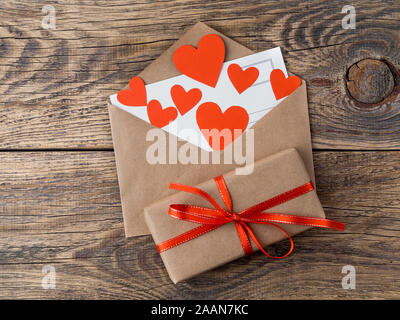 Scheda e cuori rossi in busta aperta dal marrone carta Kraft. Confezione regalo con nastro rosso in legno invecchiato sfondo vintage. Con i saluti di San Valentino da Foto Stock