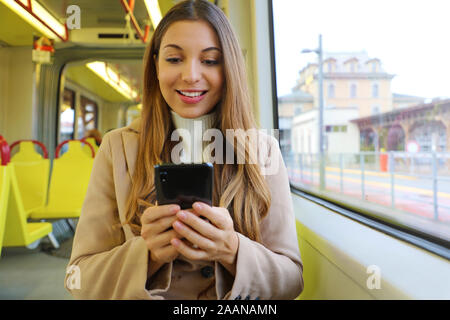 Persone su mezzi di trasporto pubblico. Sorridente giovane donna messaging con smart phone seduto sul tram. Foto Stock
