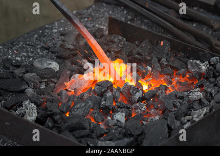 Bar riscaldamento per vaking un ferro di cavallo. Embers glow in una fucina di ferro. Incendio, calore, carbone e cenere e strumenti di fabbro. Foto Stock