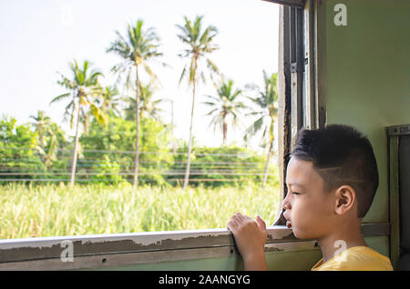 Ritratto di ragazzo asiatico sul treno finestra di sfondo vedute e alberi. Foto Stock