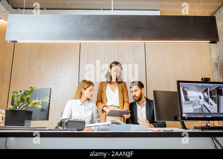 Piccolo gruppo di creativi di impiegati che lavorano insieme su alcuni progetti architettonici dell'ufficio moderno. Concetto di un patrimonio architettonico di business e il lavoro creativo Foto Stock