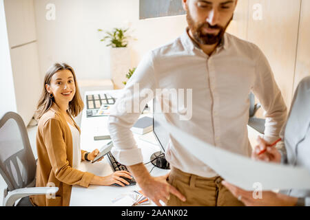 Ufficio creativo i dipendenti al lavoro su qualche progetto architettonico, tenendo blueprint e lavorare al computer in un ufficio moderno Foto Stock