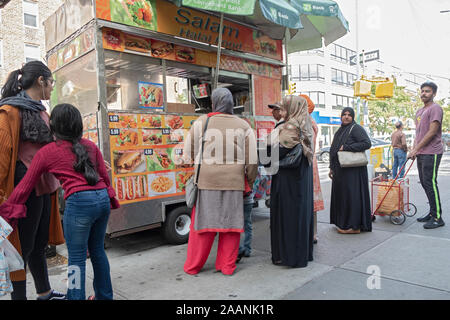 Un gruppo di persone, principalmente musulmano, line up per il cibo in un cibo Halal carrello sulla 37th Avenue a Jackson Heights, Queens, a New York City Foto Stock