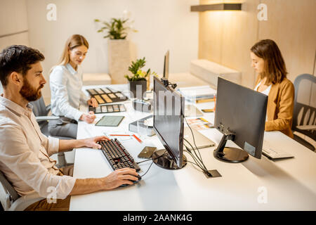 I giovani lavoratori vestito casualmente facendo qualche lavoro creativo al tavolo di grandi dimensioni con i computer in ufficio. Concetto di un patrimonio architettonico di business e il lavoro creativo Foto Stock