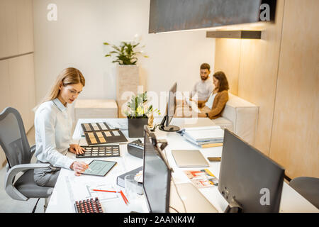 I giovani lavoratori vestito casualmente facendo qualche lavoro creativo al tavolo di grandi dimensioni con i computer in ufficio. Concetto di un patrimonio architettonico di business e il lavoro creativo Foto Stock