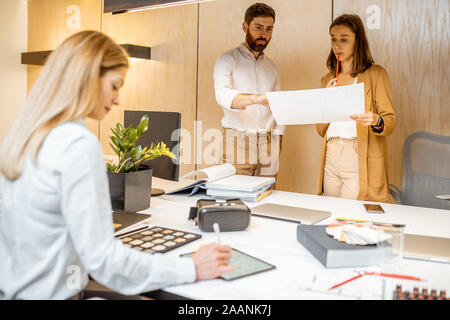 I giovani lavoratori vestito casualmente facendo qualche lavoro creativo al tavolo di grandi dimensioni con i computer in ufficio. Concetto di un patrimonio architettonico di business e il lavoro creativo Foto Stock