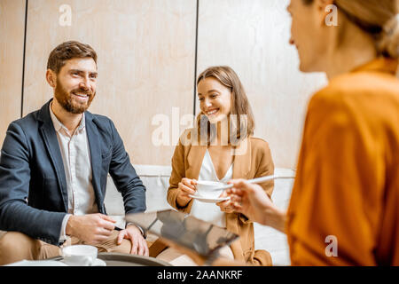 Coppia giovane di parlare con un responsabile delle vendite o agente immobiliare, offrendo alcuni prodotti con una tavoletta digitale in ufficio Foto Stock