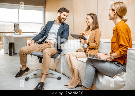 Giocoso uomo flirtare con giovani colleghi, le donne sedute e lavorare sul lettino in ufficio Foto Stock