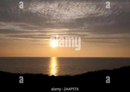 Untergehende Sonne zwischen Meer und Wolken am Strand bei Wenningstedt auf Sylt Foto Stock