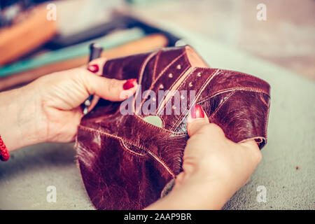 Close up di una femmina di calzolaio lavora con cuoio utilizzando gli strumenti di creazione. Procedimento per la fabbricazione di parti di calzature. Messa a fuoco selettiva Foto Stock