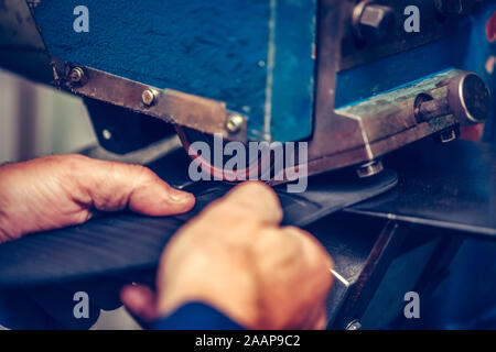 Le mani di un calzolaio esperto utilizzando una speciale macchina utensile per la realizzazione di calzature. Pattino del processo di produzione in fabbrica. Messa a fuoco selettiva Foto Stock