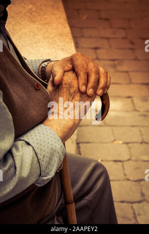 Il vecchio uomo seduto e tenendo un bastone Foto Stock