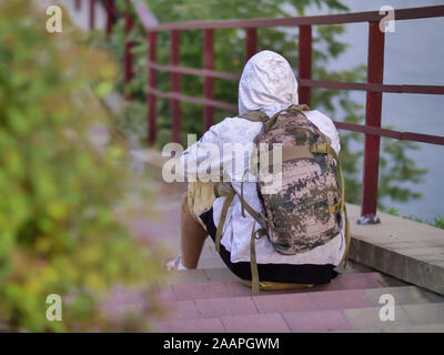 Lonely ragazzo con uno zaino e una cappa si siede sui gradini della scala nel parco Foto Stock