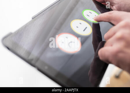 Lieta persona che fornisce il feedback positivo toccando Smiley face sulla tavoletta digitale touchscreen, la qualità del servizio il concetto di rating. Foto Stock