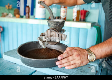 Cuba: Uomo di grind con un vecchio mulino di caffè Foto Stock