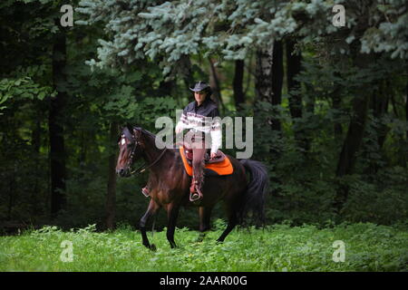 Bella bionda cowgirl in sella ad un cavallo marrone. Foto Stock