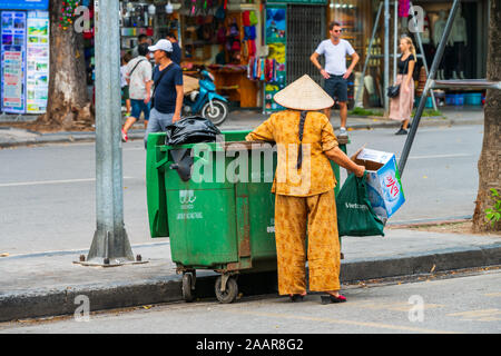 Hanoi, Vietnam - XII Ottobre 2019: una donna asiatica trasporta rifiuti e immondizie fuori del verde del bidone dei rifiuti nelle strade di Hanoi, Vietnam Asia Foto Stock