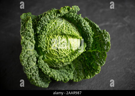 Un intero British cavolo verza acquistato da un supermercato nel Regno Unito. Fotografato al buio su un sfondo di ardesia. Inghilterra REGNO UNITO GB Foto Stock