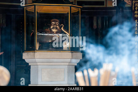 Bastoncini di incenso bruciare davanti alla statua dorata del Buddha Sorridente nel Thien Mu pagoda in tinta. Foto Stock