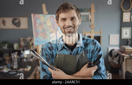 Ritratto di giovane artista barbuto in maglietta controllato con un tubo di fumo in un atelier di pittura Foto Stock