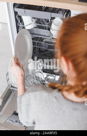 Lavori di casa: giovane donna di mettere i piatti in lavastoviglie Foto Stock