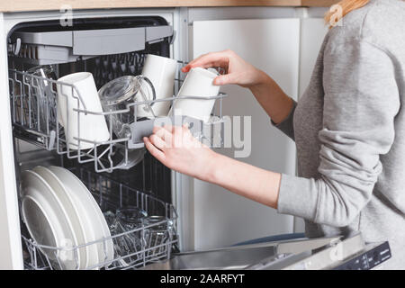 Lavori di casa: giovane donna di mettere i piatti in lavastoviglie Foto Stock