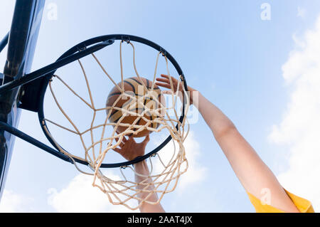 Ragazzo giovane facendo una Slam Dunk in street basket con cielo blu e nuvole bianche Foto Stock