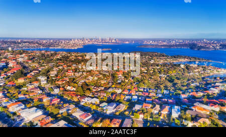 Sobborghi Orientali di Sydney in vista aerea attraverso Sydney Harbour verso città lontana CBD alti torri e waterfront sotto soft. La luce del mattino su un Foto Stock